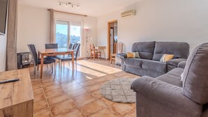 A living room with a grey sofa, a dining table with chairs, and a large window. - Villa Luz Lloret with Pool (Lloret De Mar)