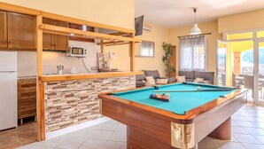 A pool table in a well-lit room with a kitchen area, a sofa, and a view of the outdoors. - Villa Luz Lloret with Pool (Lloret De Mar)