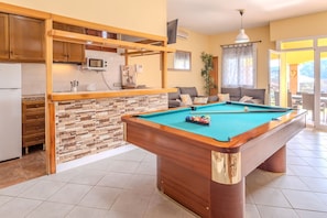 A pool table in a well-lit room with a kitchen area, a sofa, and a view of the outdoors. - Villa Luz Lloret with Pool (Lloret De Mar)