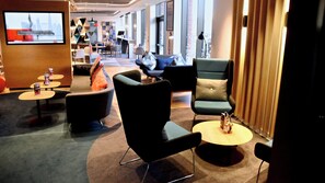 A modern hotel lobby with a mix of seating options including sofas, armchairs, and round tables. There are multiple tables with small items on them, and a television screen is mounted on the wall. - Holiday Inn Express Barrow In Furness (Barrow-in-Furness)