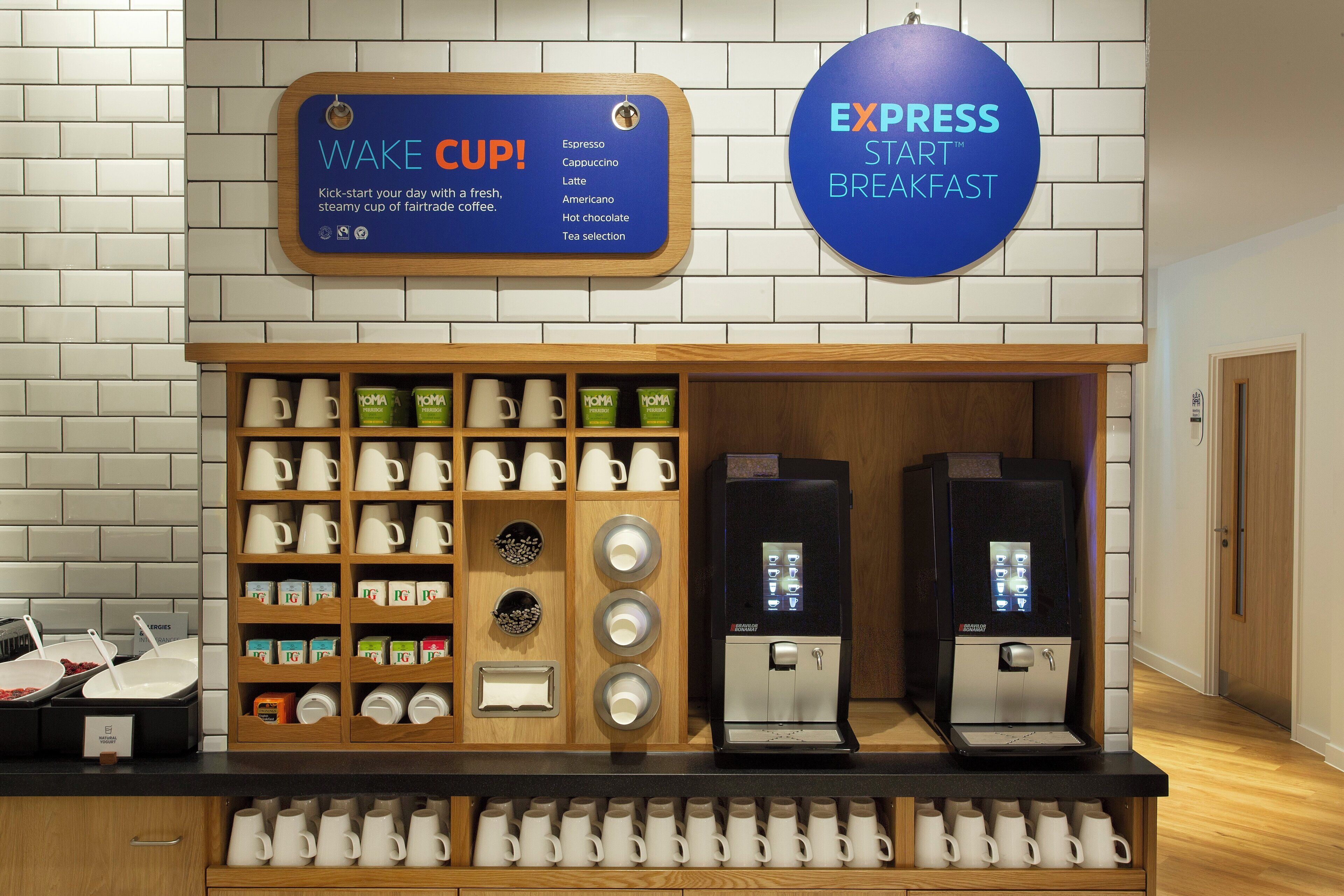 A coffee station with a sign for 'Wake Cup' and 'Express Star Breakfast,' a coffee machine, and a variety of coffee cups and mugs.