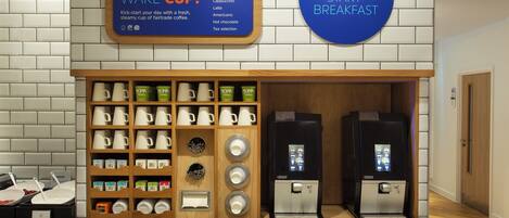 A coffee station with a sign for 'Wake Cup' and 'Express Star Breakfast,' a coffee machine, and a variety of coffee cups and mugs.