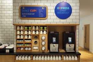 Una estación de café con un cartel que dice 'Wake Cup' y 'Express Star Breakfast', una máquina de café y una variedad de tazas y vasos.