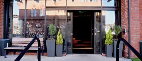 A building entrance with a glass door, a bench, and two potted plants.