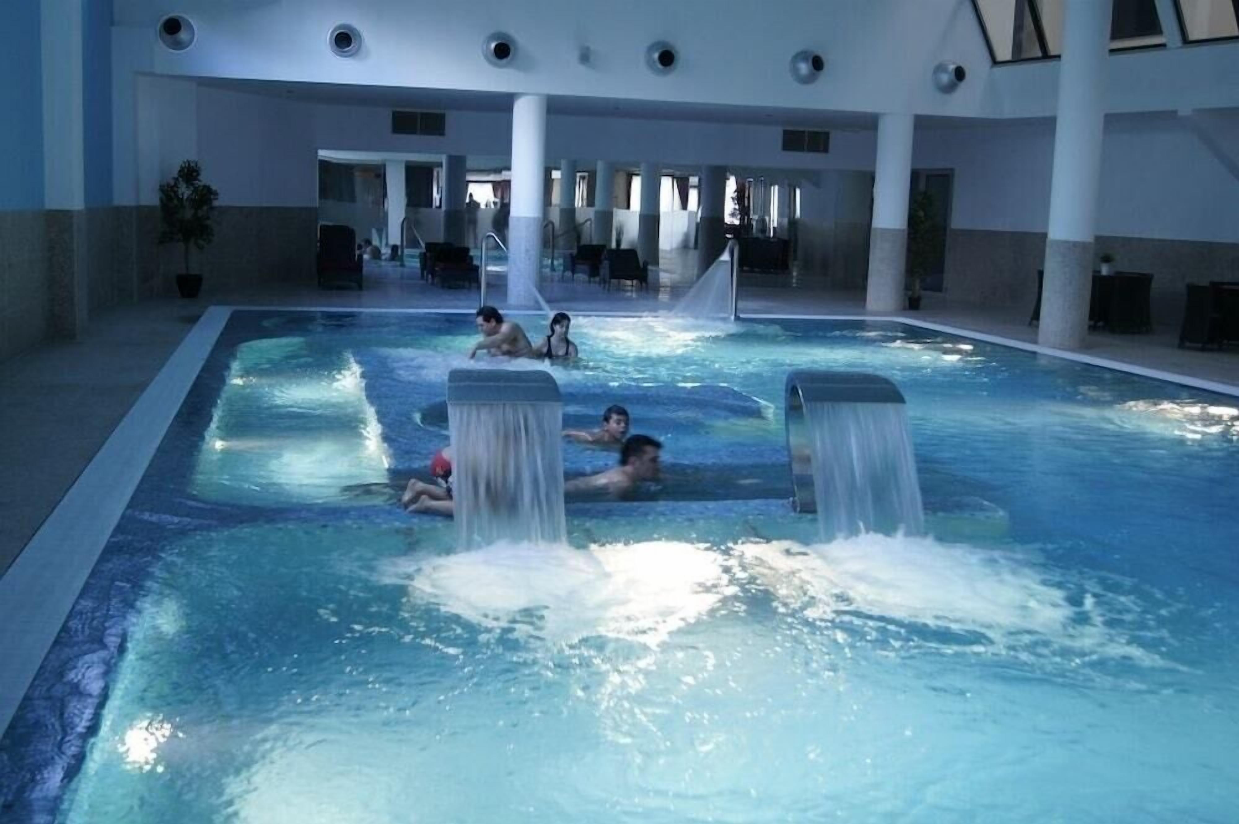 An indoor swimming pool with multiple water jets, lounge chairs, and a spacious layout.