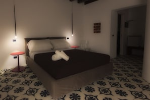 A hotel room with a bed, two bedside tables, a red table, a patterned floor, and a small wall-mounted shelf. - Antichi Ricordi DE Charme E SPA (Caltanissetta)