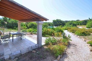 Un patio al aire libre con una pérgola, pilares de piedra y una mesa con sillas.