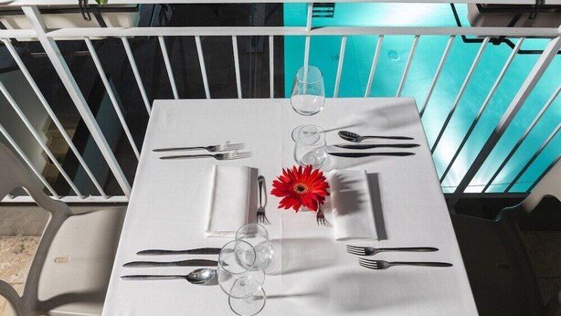 A table set for two with white tablecloth, clear glasses, cutlery, and a red flower. - The Florence Hills Resort Spa (Pelago)