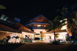 A modern hotel with a central atrium, surrounded by lush greenery and palm trees.