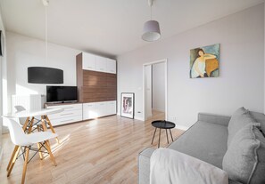 A modern living room with a grey sofa, a dining table with chairs, a flat-screen TV, and a painting on the wall. - Business Mokotów Park 23 Studio (Warszawa)