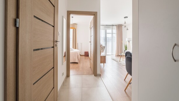 Un couloir d’hôtel moderne avec des portes en bois, un lit, un bureau et une chaise.
