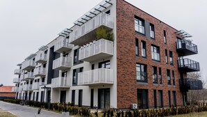 Un immeuble moderne à plusieurs étages, doté de balcons, d’une façade en briques et d’un trottoir dallé.