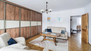 Een ruime woonkamer met houten vloer, een bank, een salontafel en een groot raam met houten lambrisering.