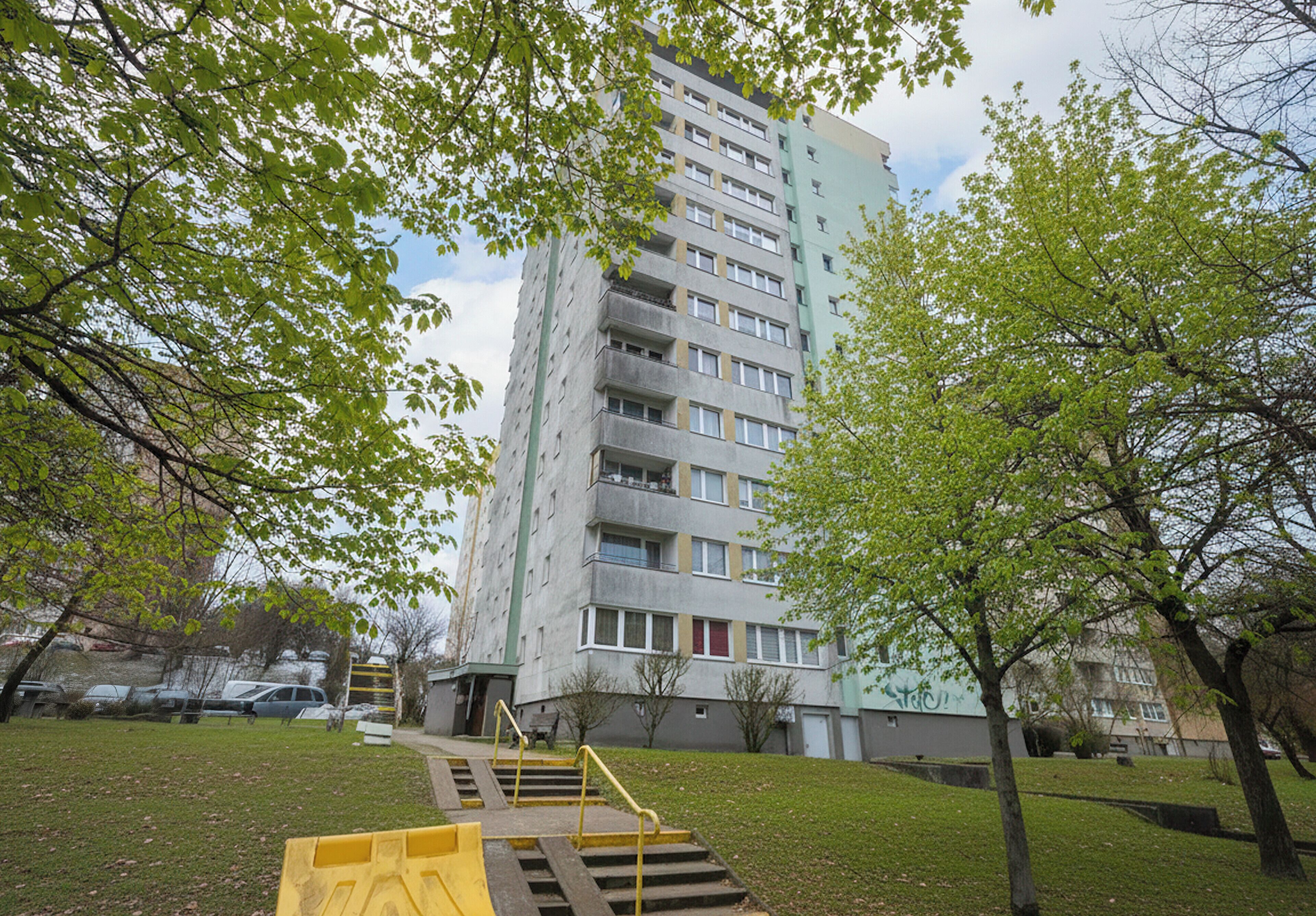 A multi-story building with a staircase leading to the entrance, surrounded by trees and a grassy area.