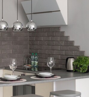 Een moderne keuken met een grijze tegelwand, roestvrijstalen apparatuur en een bar voorzien van glazen en flessen.