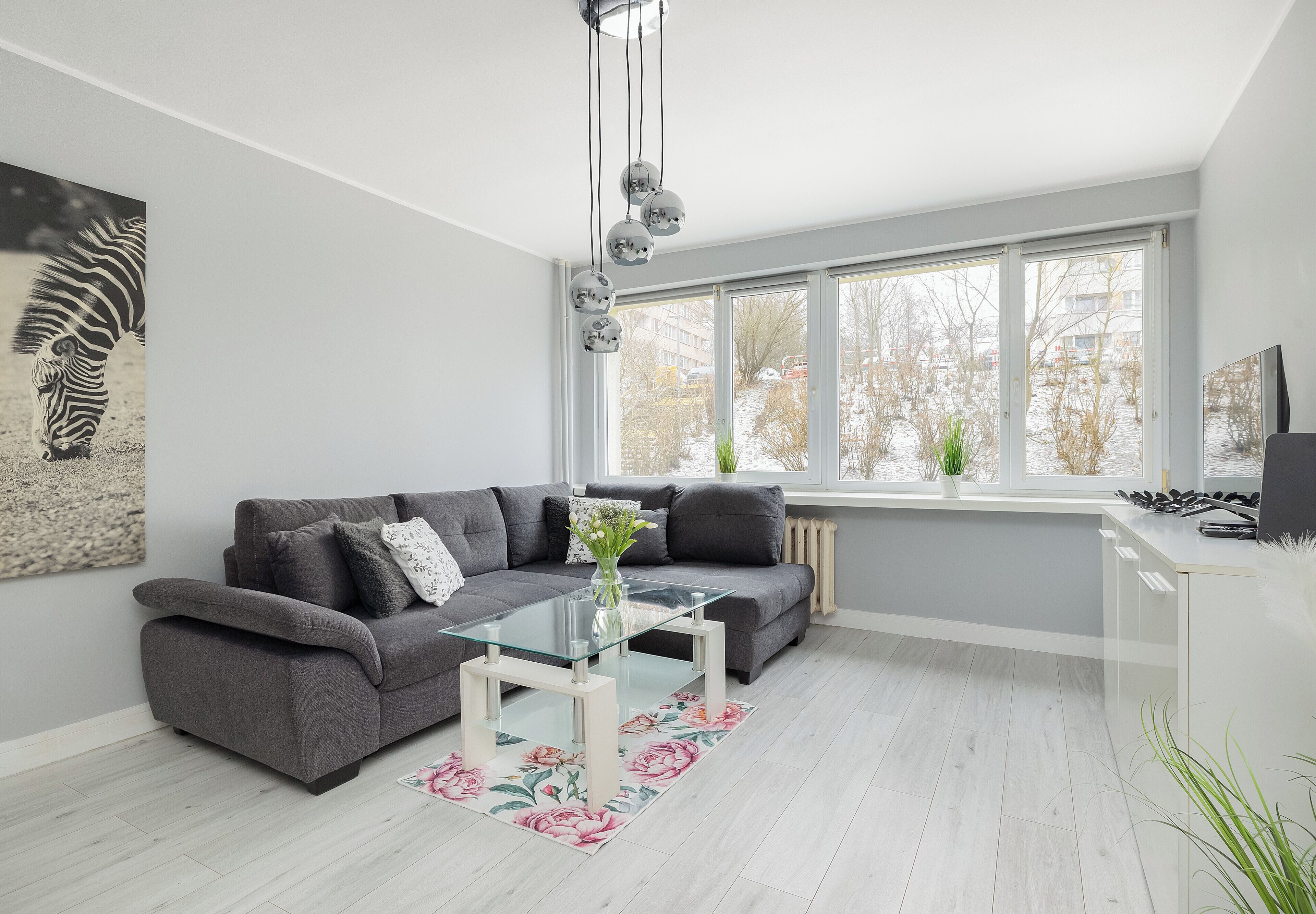 Un salon moderne avec un canapé gris, une table basse en verre et une grande fenêtre donnant sur un paysage enneigé.