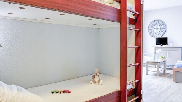 Una cama litera con escalera, un osito de peluche y coches de juguete sobre el colchón.
