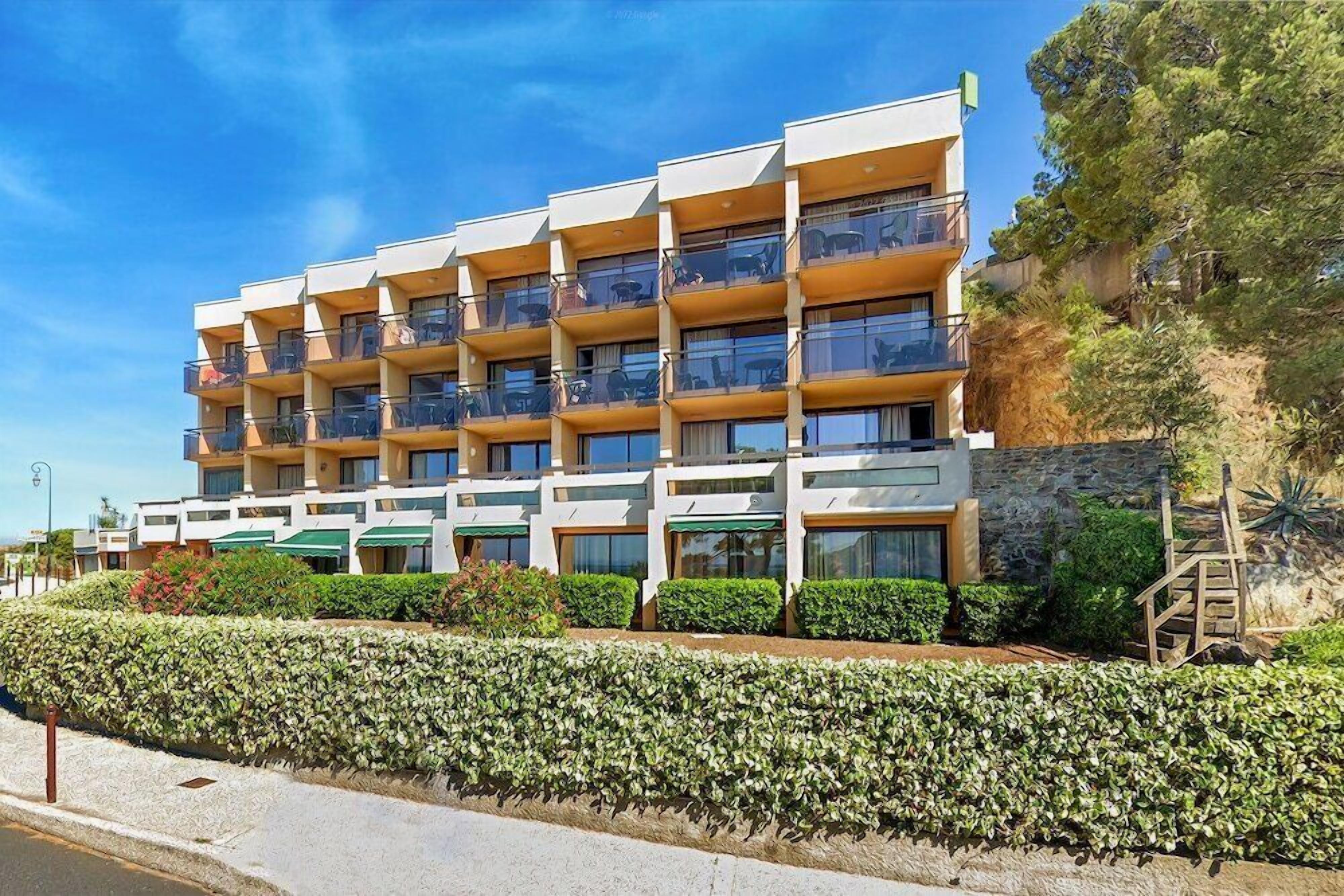 A multi-story hotel with balconies, a stone facade, and a landscaped garden.