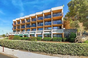 Un hôtel à plusieurs étages, doté de balcons, d’une façade en pierre et d’un jardin aménagé.