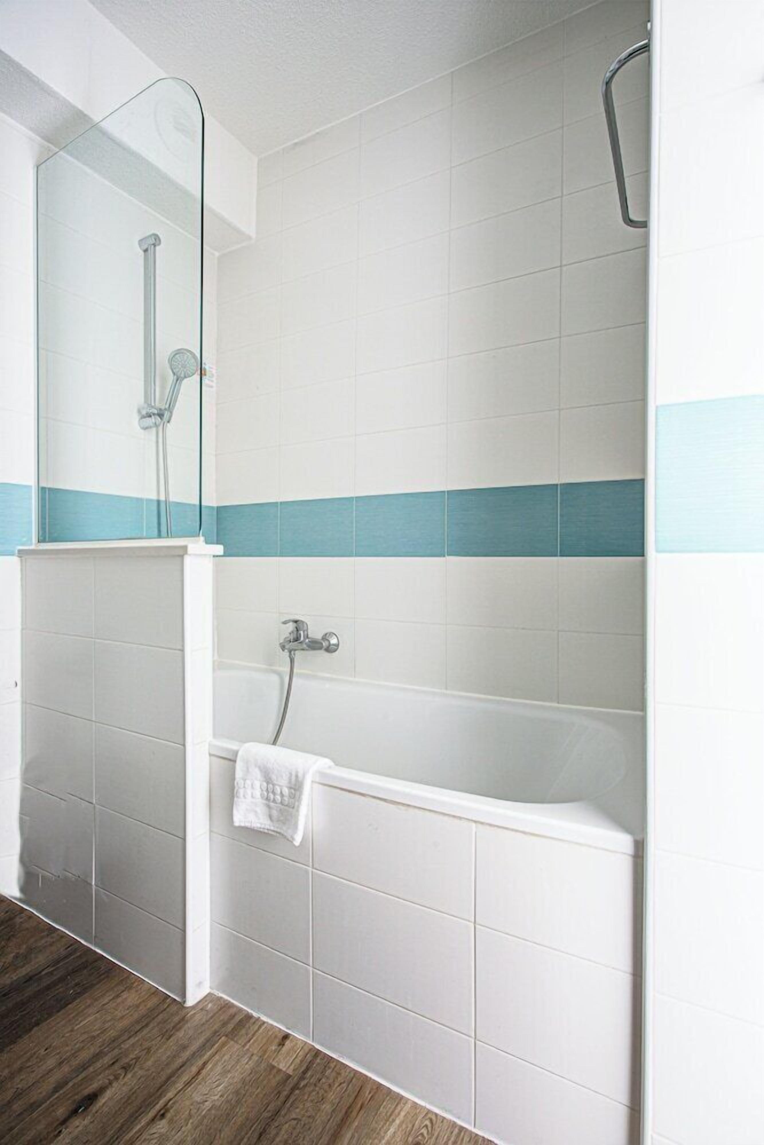A bathroom with a glass shower enclosure, a bathtub, and a towel hanging on the wall.