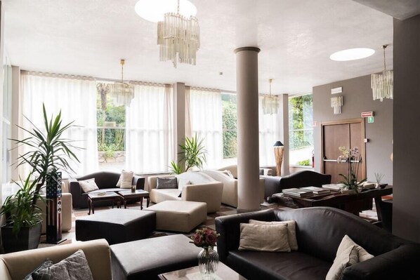 A spacious living room with a large window, a chandelier, and a coffee table. - Giardinetto (Pettenasco)