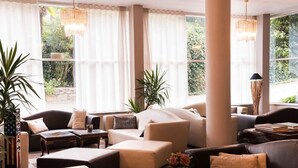 A spacious living area with multiple sofas and armchairs, large windows with sheer curtains, and potted plants. - Giardinetto (Pettenasco)