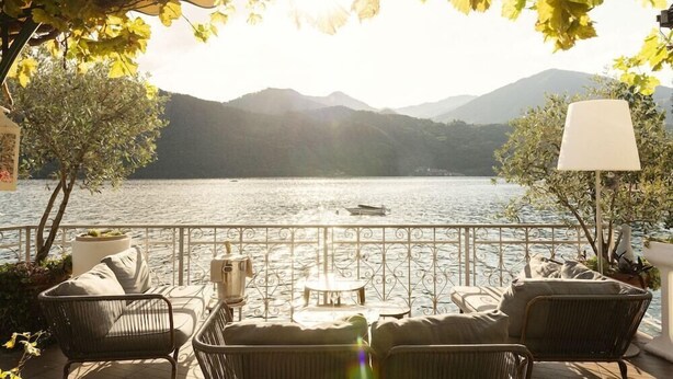 A terrace with wicker furniture, a table, and a lamp, overlooking a lake with mountains in the background. - Giardinetto (Pettenasco)