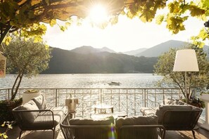A terrace with wicker furniture, a table, and a lamp, overlooking a lake with mountains in the background. - Giardinetto (Pettenasco)