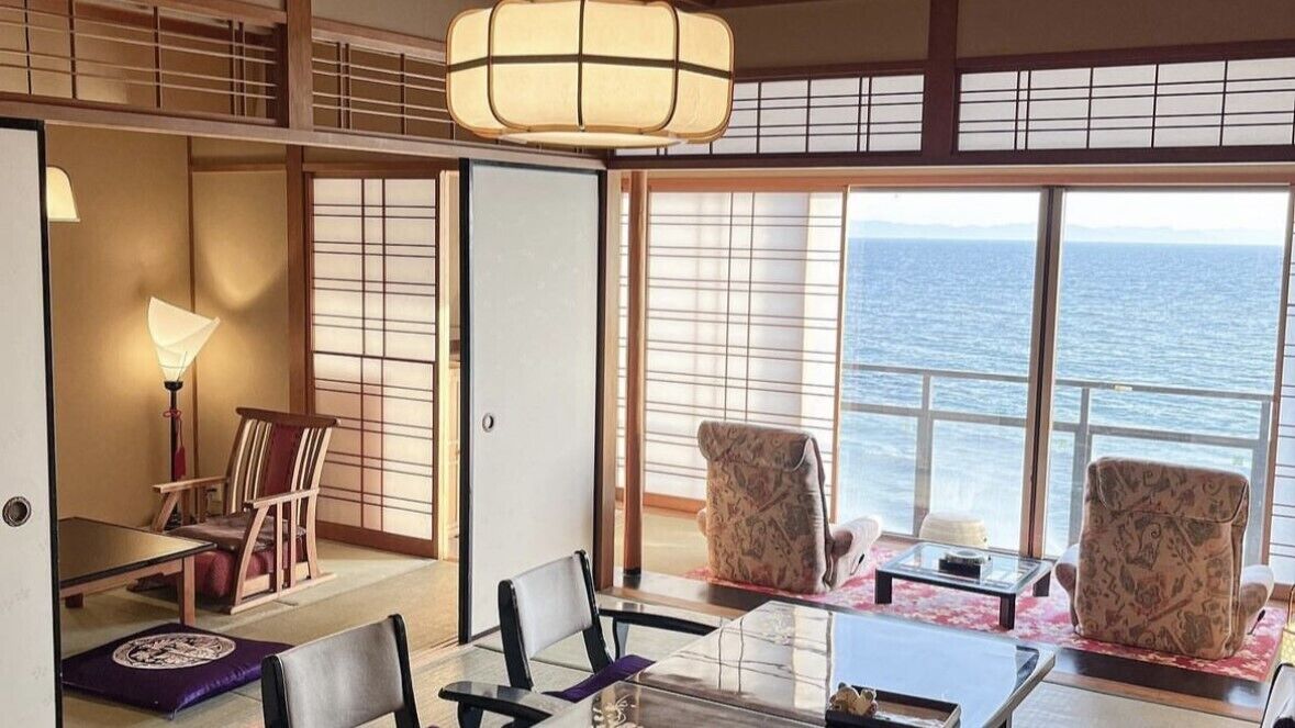 A room with a view of the sea, traditional Japanese sliding doors, a table with chairs, and a hanging light fixture.