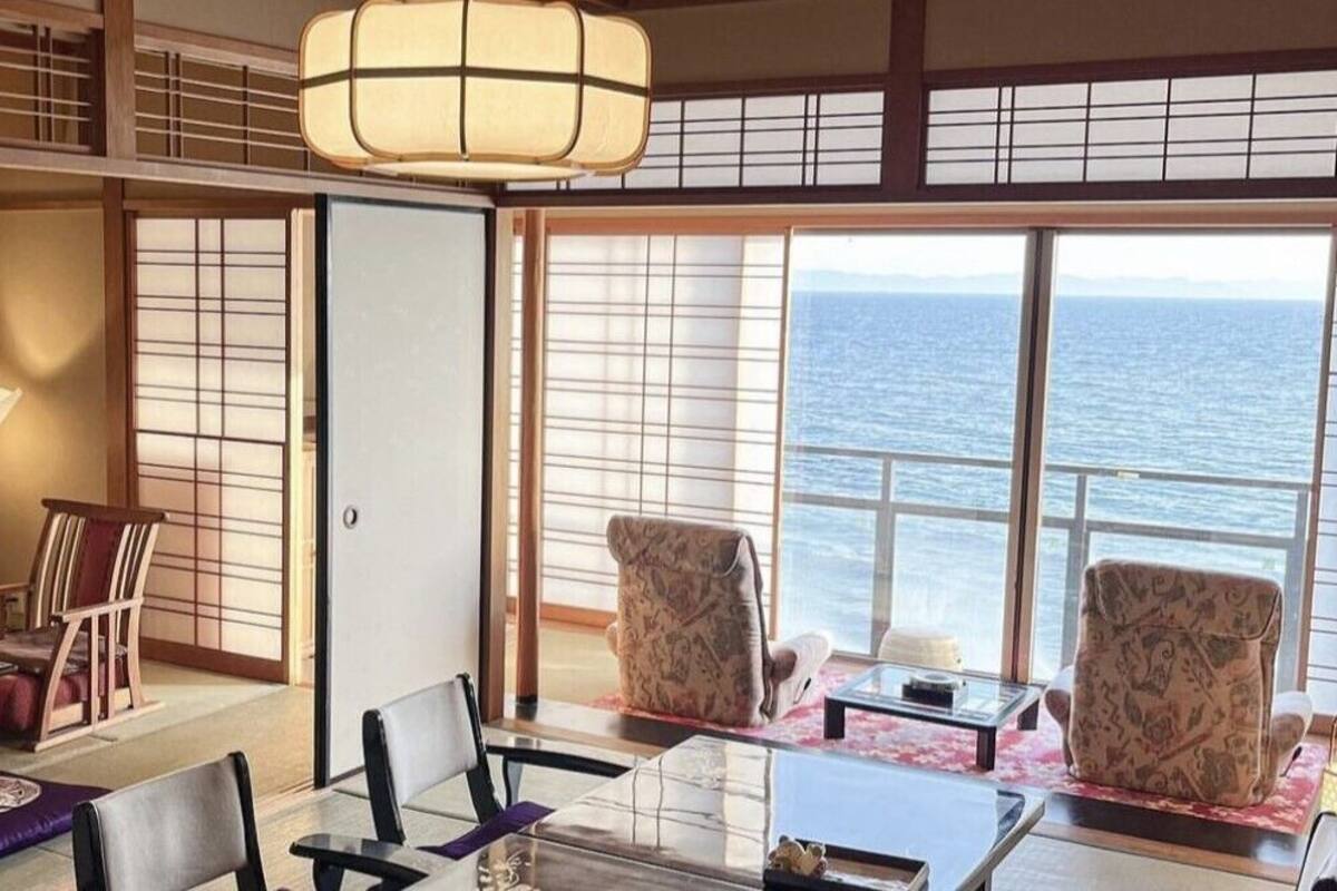 A room with a view of the sea, traditional Japanese sliding doors, a table with chairs, and a hanging light fixture.