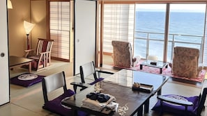A room with a dining table, chairs, a sofa, a lamp, and a view of the sea. - Shukukaifu (Minamichita)