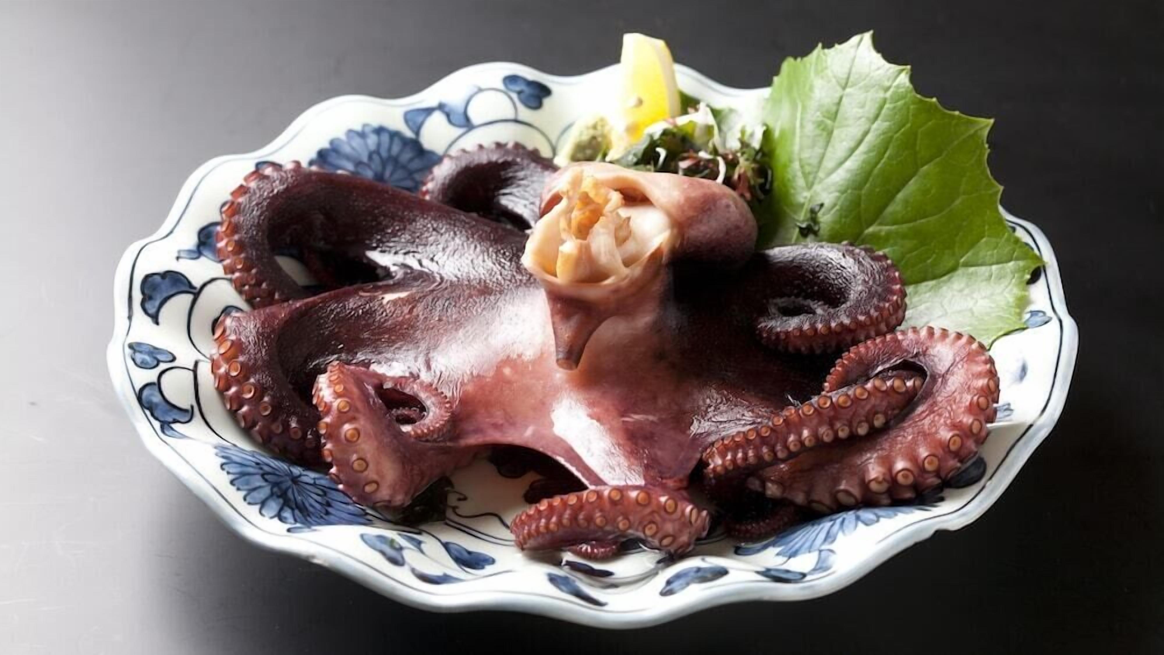 A plate with octopus tentacles, a lemon wedge, and a green leaf.