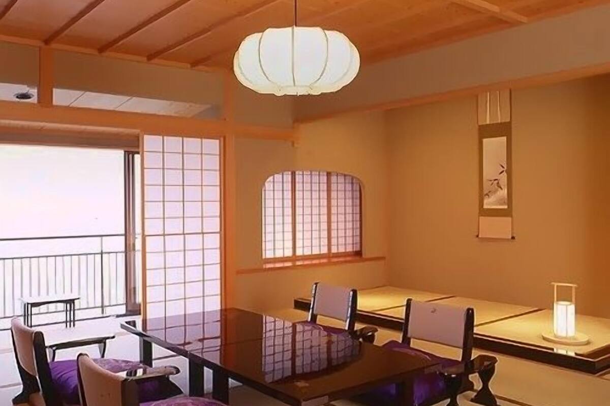 A traditional Japanese room with tatami flooring, a low table, and a hanging light fixture.