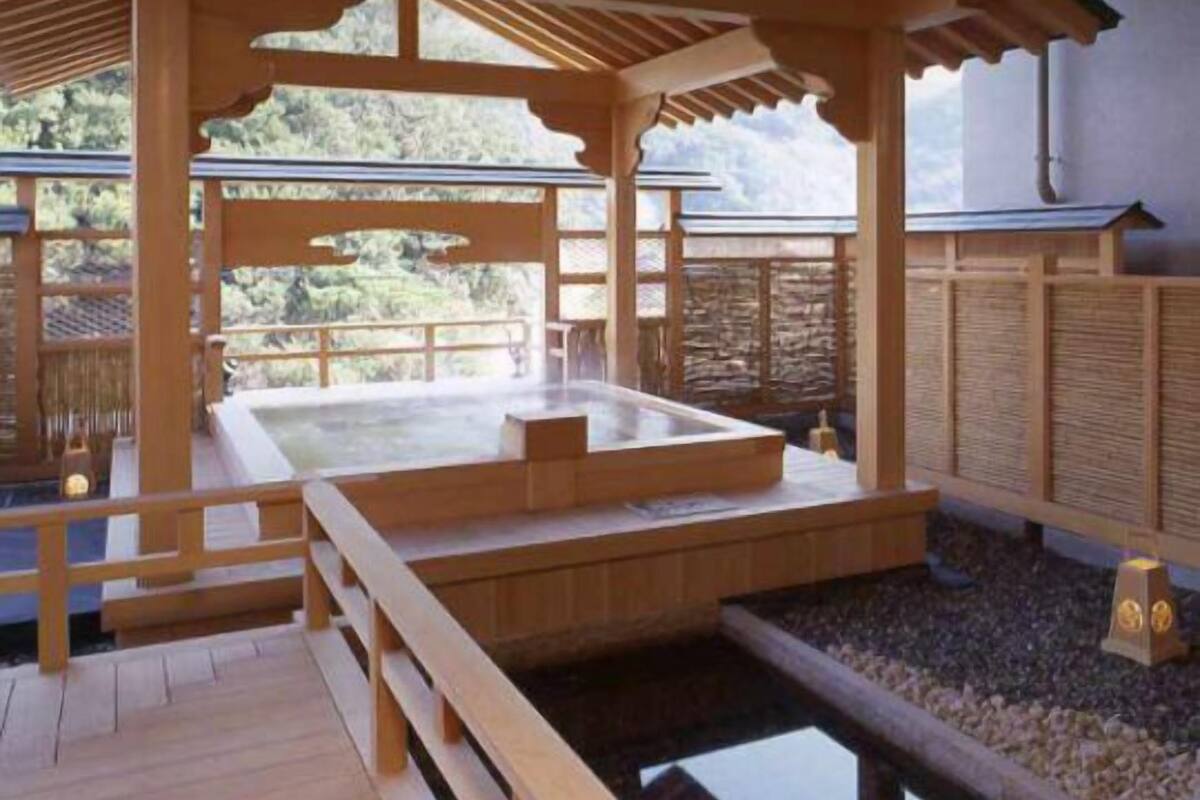 A traditional wooden bathhouse with a hot spring, wooden benches, and a view of the surrounding landscape.