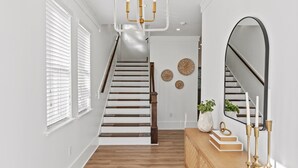 Een trap met houten treden en witte wanden, leidend naar een plateau met een spiegel en decoratieve objecten.