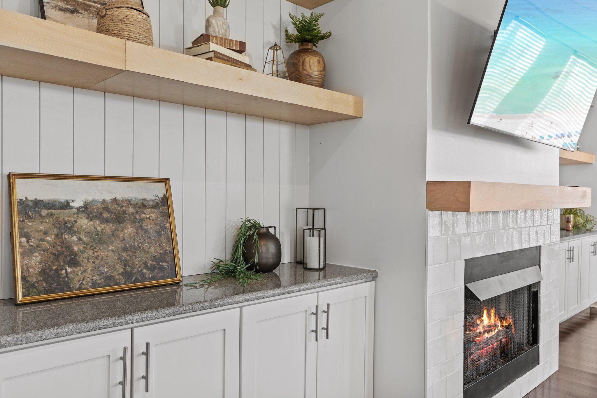 A modern living room with a fireplace, wooden shelves, a television, and a framed picture.