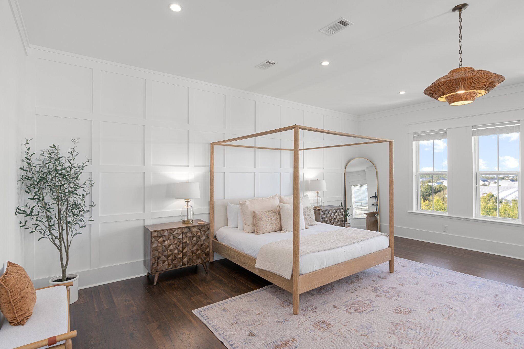 A modern bedroom with a four-poster bed, a large mirror, and a view of the outdoors through the window.