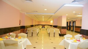A banquet hall with rows of tables set for a formal event, featuring white tablecloths and gold sashes. - Sama Al Deafah (Makkah)