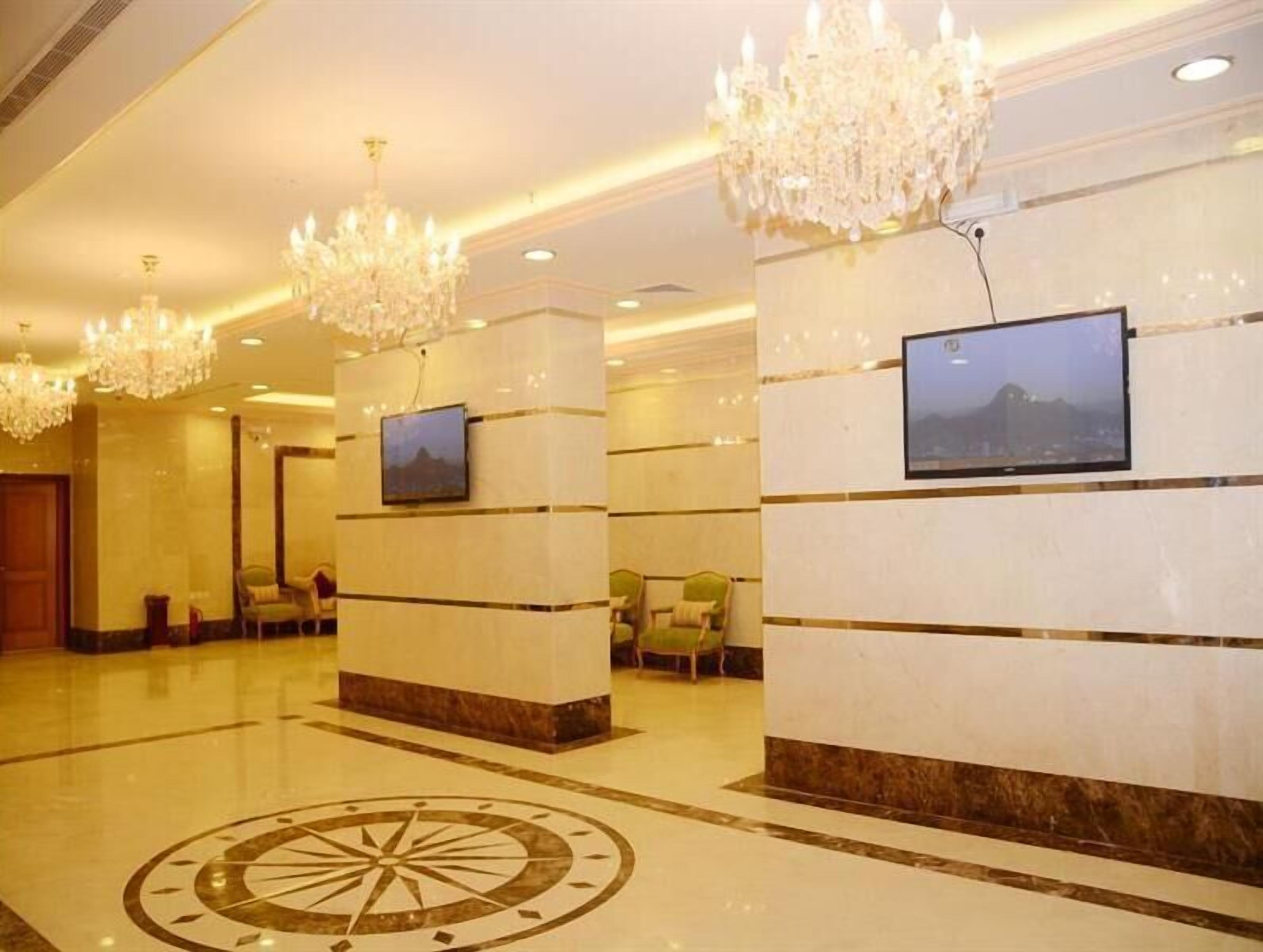 A lobby with chandeliers, a TV mounted on the wall, and a large circular floor design.