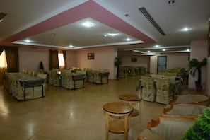 A spacious indoor area with multiple tables and chairs, some covered with tablecloths, and a few potted plants. - Riyadh Al Deafah (Makkah)