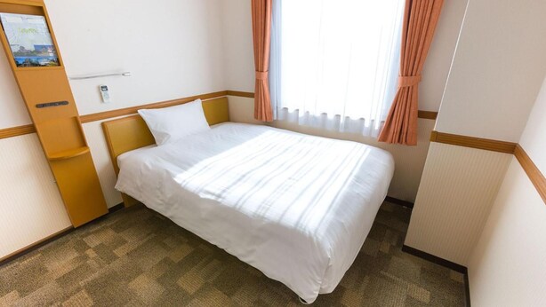 A hotel room with a bed, a wooden nightstand, a small table, and a window with curtains. - Toyoko INN Yokohama-sen Fuchinobe-eki Minami-guchi (Sagamihara)