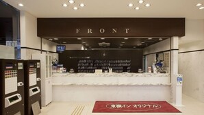 A hotel reception area with a marble counter, a clock, and a television above it. There are vending machines to the left and a red carpet with Japanese text in the center. - Toyoko INN Yokohama-sen Fuchinobe-eki Minami-guchi (Sagamihara)