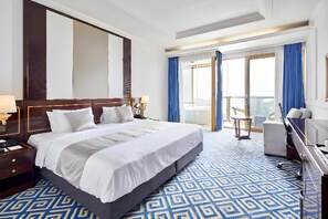 Ein Hotelzimmer mit einem großen Bett, einem Schreibtisch, einem Sessel und einem Balkon mit Vorhängen.