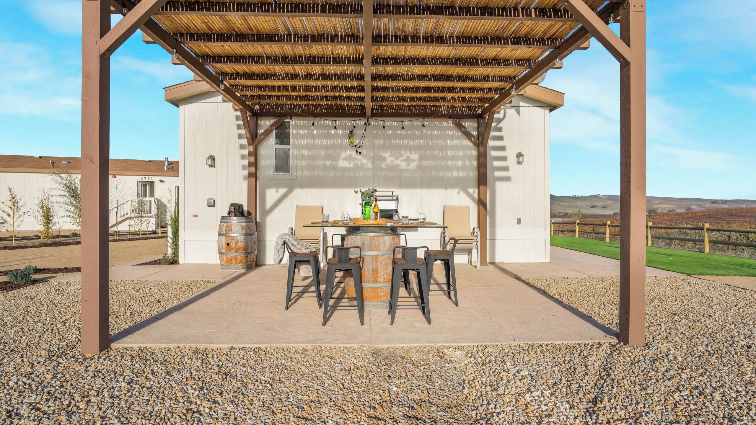 An outdoor patio with a pergola, a table with chairs, and a rustic barrel.