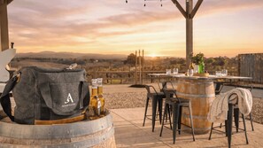 Une table dressée à l’extérieur, avec vue sur la campagne, un tonneau et un sac sur lequel on peut lire « AVANTSTAY ».