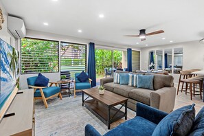 A spacious living area with a sofa, chairs, and a dining table. Large windows with blinds provide views of greenery outside. - New Listing! Modern Garden Oasis in West Maui (Honokowai)