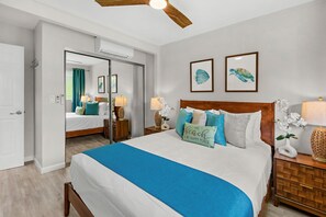 A bedroom with a large bed, a wooden headboard, two framed wall art pieces, a bedside table with a lamp, and a nightstand with a lamp. - New Listing! Modern Garden Oasis in West Maui (Honokowai)