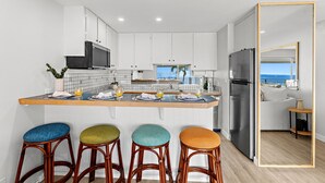 A modern kitchen with white cabinets, a central island with bar stools, a stainless steel refrigerator, and a view of the sea through the window. - New Listing! Ocean Front Gem in Lahaina (Lahaina)