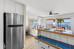 A modern kitchen with a stainless steel refrigerator, a wooden countertop, and a view of the ocean through large windows. - New Listing! Ocean Front Gem in Lahaina (Lahaina)