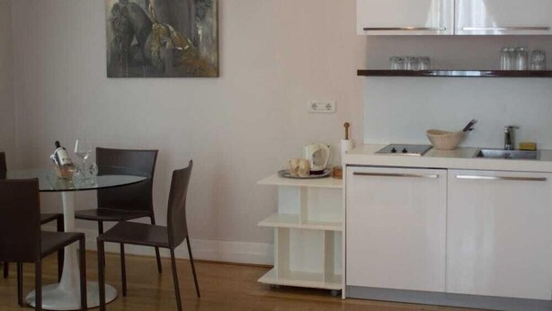 A modern kitchen with white cabinets, a glass dining table, and a painting on the wall. - Olea (Dubrovnik)